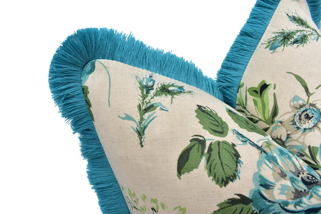 A close-up view of a decorative pillow with a floral pattern and a blue fringe trim.