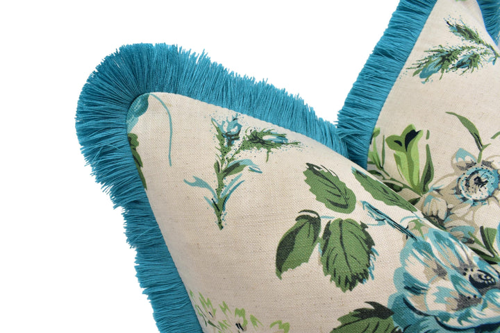 A close-up view of a decorative pillow with a floral pattern and a blue fringe trim.