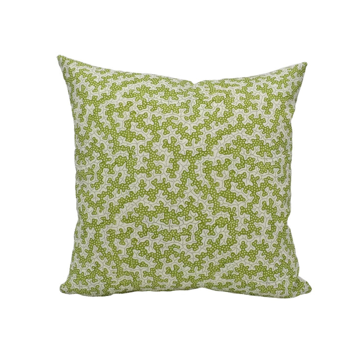 A square throw pillow with a green floral pattern is placed against a white wall.