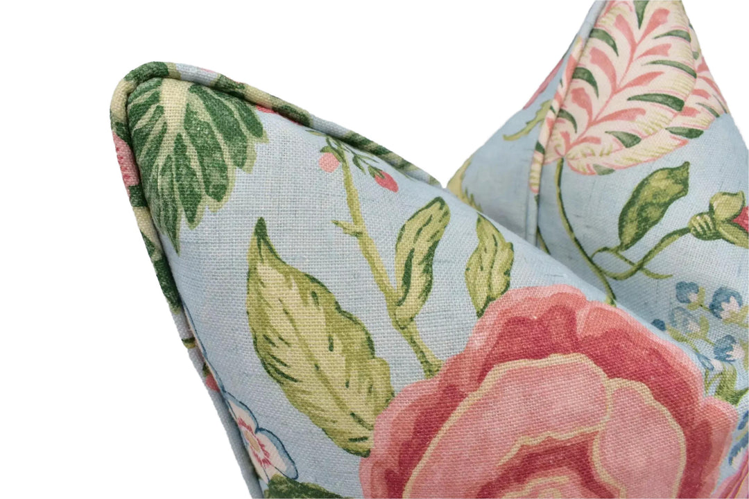 a close-up view of a decorative pillow with a floral pattern. The pillow has a light blue background with green leaves and pink flowers, creating a visually appealing and colorful design.