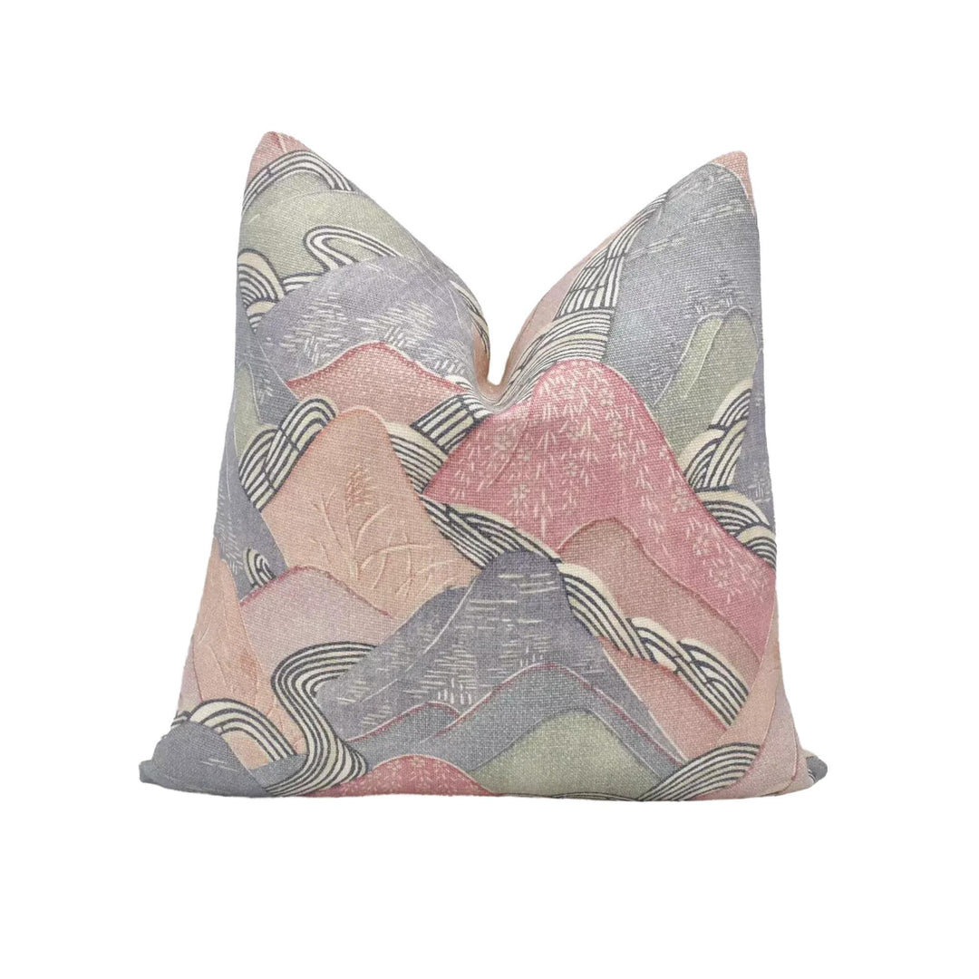 a decorative pillow with a mountain landscape design in shades of pink, gray, and white.