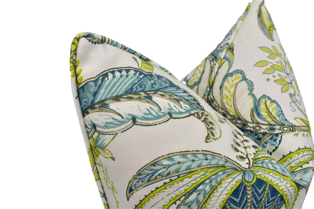 a close-up view of two decorative pillows with a tropical leaf pattern in shades of green and blue.