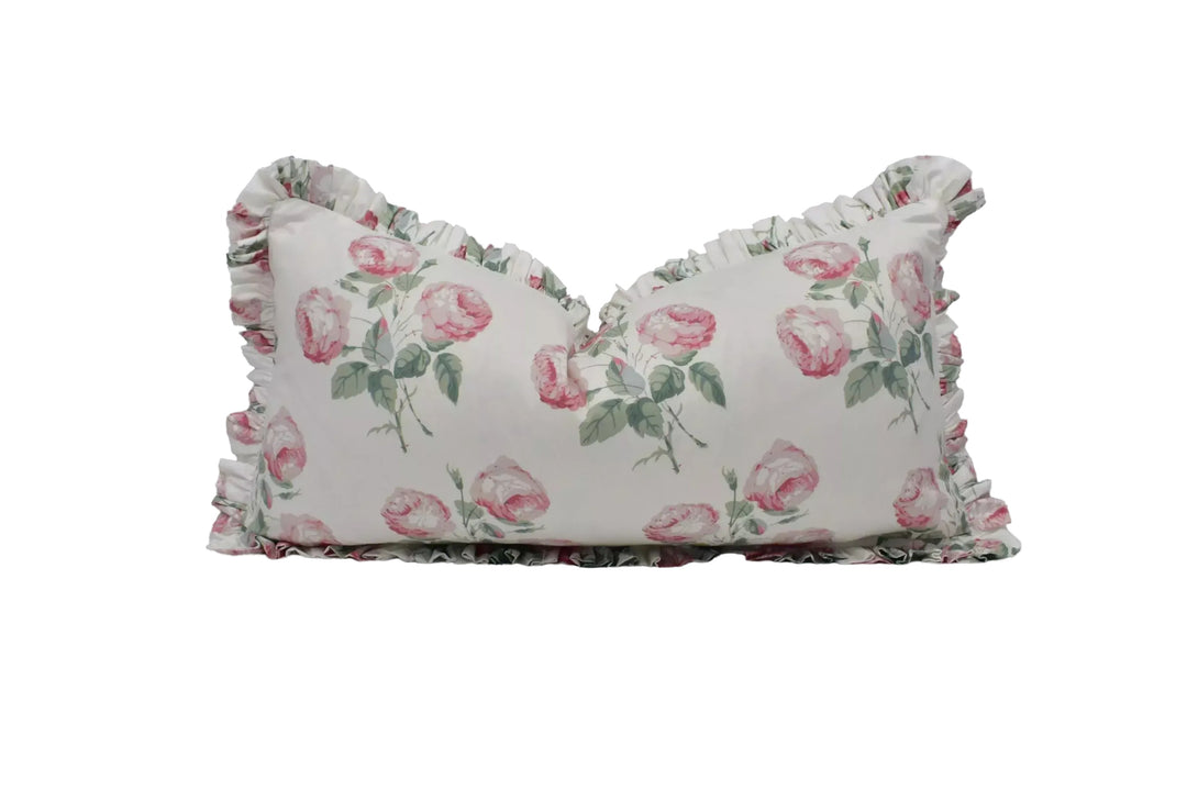 A white pillow with a floral print of pink roses on it, featuring a ruffled trim around the edges.