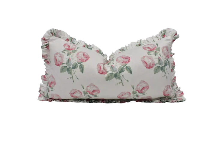 A white pillow with a floral print of pink roses on it, featuring a ruffled trim around the edges.