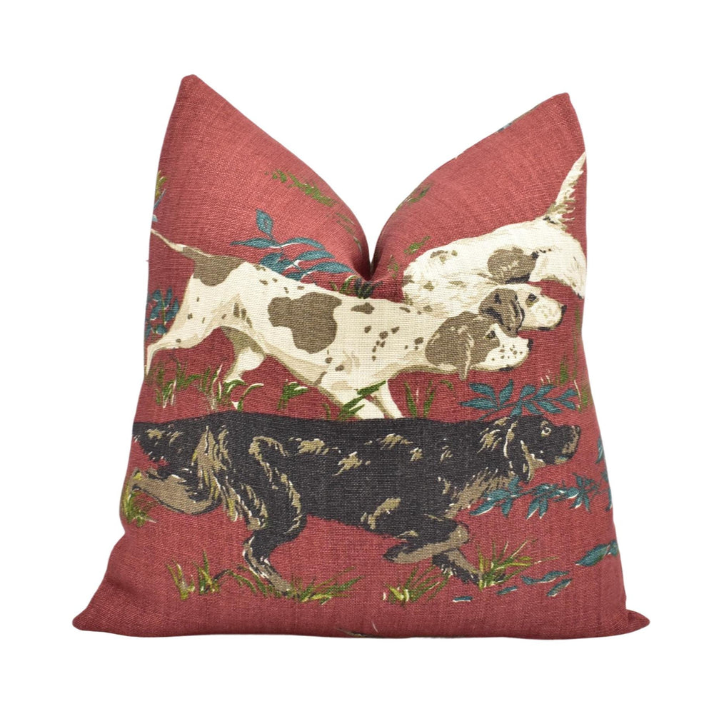 a red pillow with a design of two dogs, one black and one brown, walking through a grassy field.