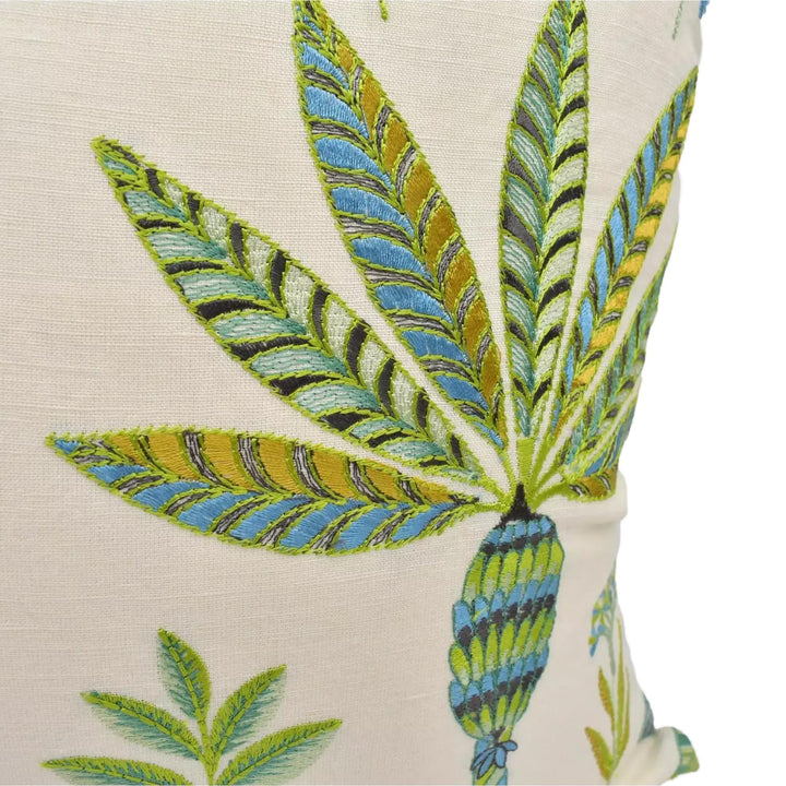 a close-up view of a decorative pillow with a tropical leaf design. The leaf pattern is vibrant and colorful, with a mix of green, blue, and yellow hues. The design is intricate and detailed, showcasing the craftsmanship involved in creating the pillow.