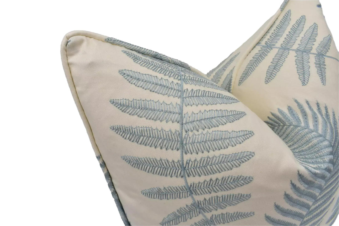 a close-up view of a decorative pillow with a repeating pattern of fern leaves in shades of blue and white.