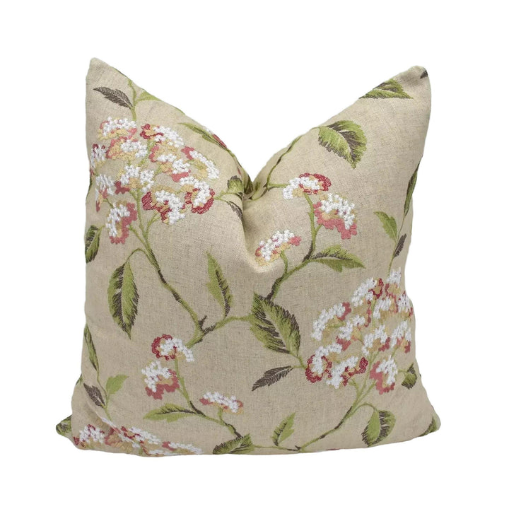 A beige pillow with a floral print design, featuring white and pink flowers and green leaves.