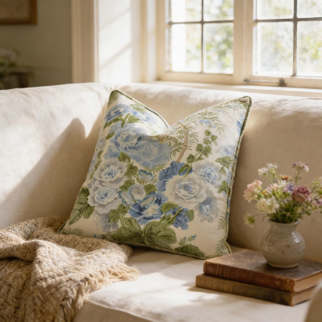 a cozy living room with a white sofa adorned with a floral throw pillow, a stack of books, and a vase of flowers on a small table.