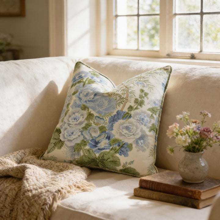 a cozy living room with a white sofa adorned with a floral throw pillow, a stack of books, and a vase of flowers on a small table.