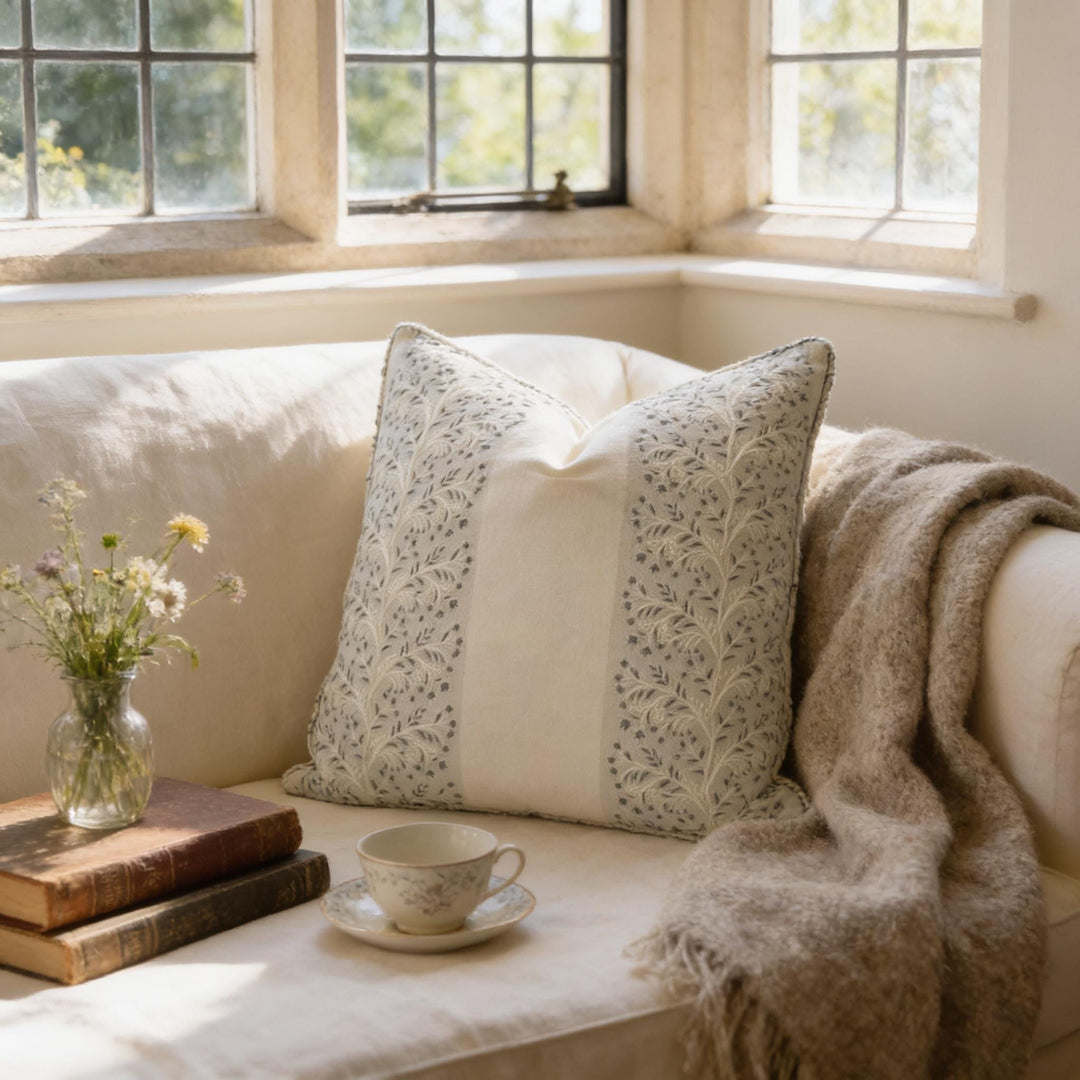 A cozy living room scene with a white sofa, a decorative pillow, a vase of flowers, a stack of books, and a cup of tea on a saucer.