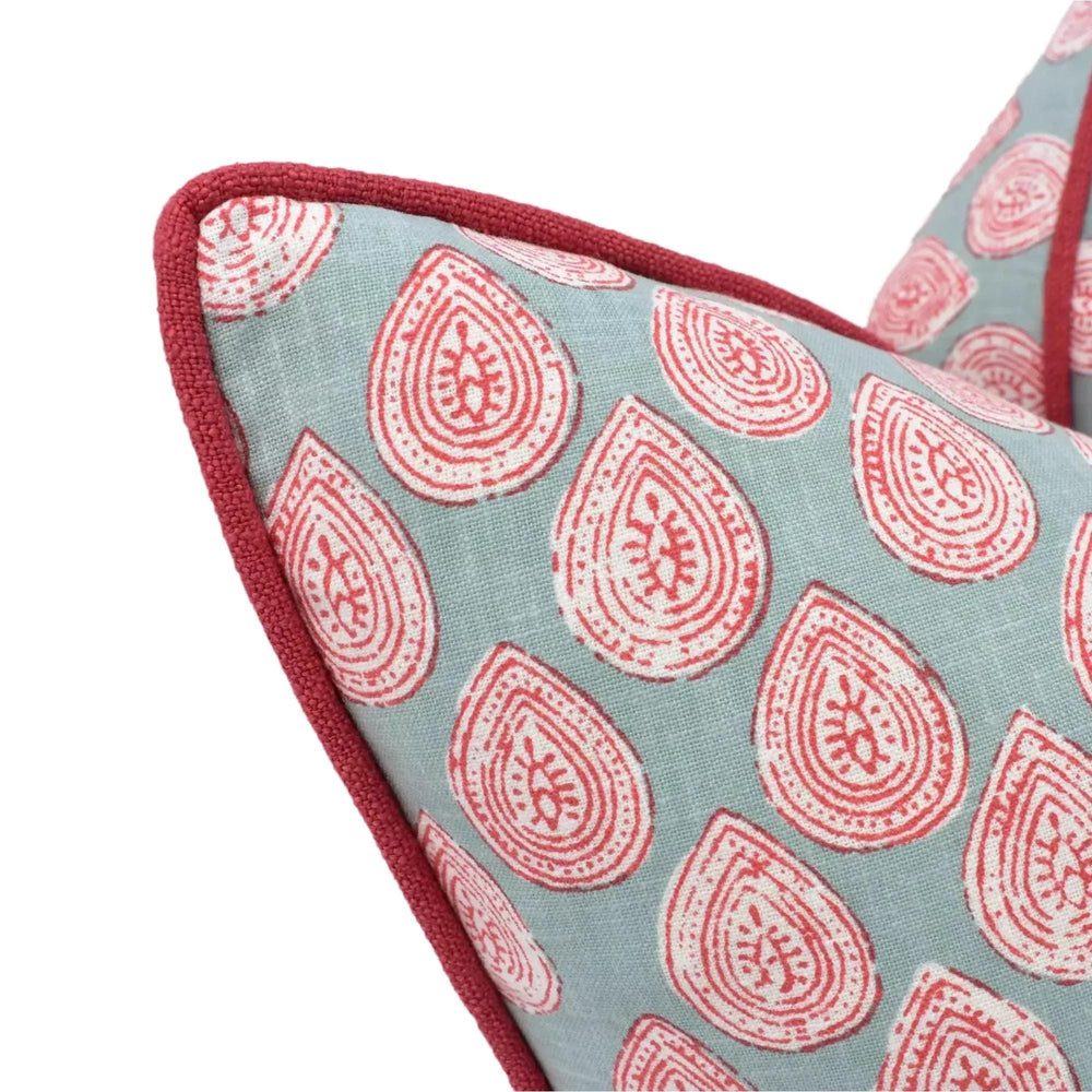 a close-up view of a decorative pillow with a repeating pattern of red and white teardrop shapes on a light blue background.
