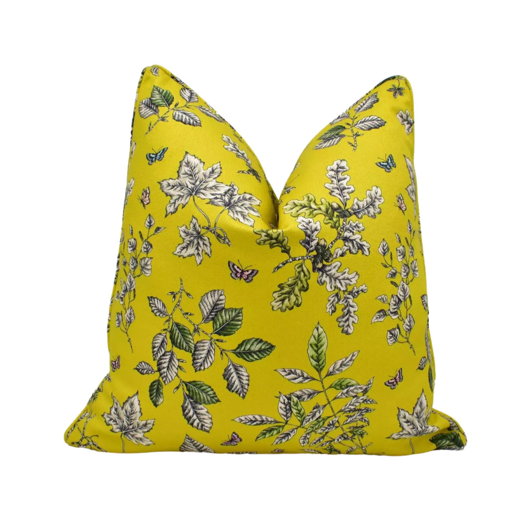 A yellow pillow with a floral print design featuring white flowers, leaves, and butterflies.
