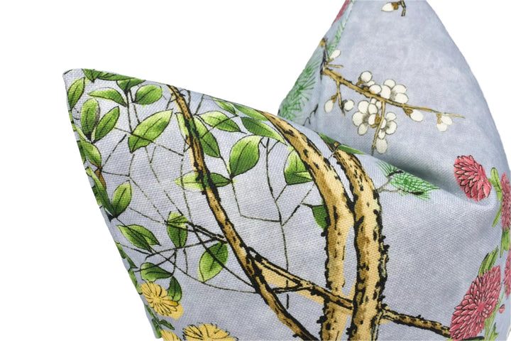 a close-up view of a decorative pillow with a floral pattern. The pillow has a combination of green leaves, yellow flowers, and brown tree branches, creating a visually appealing design.