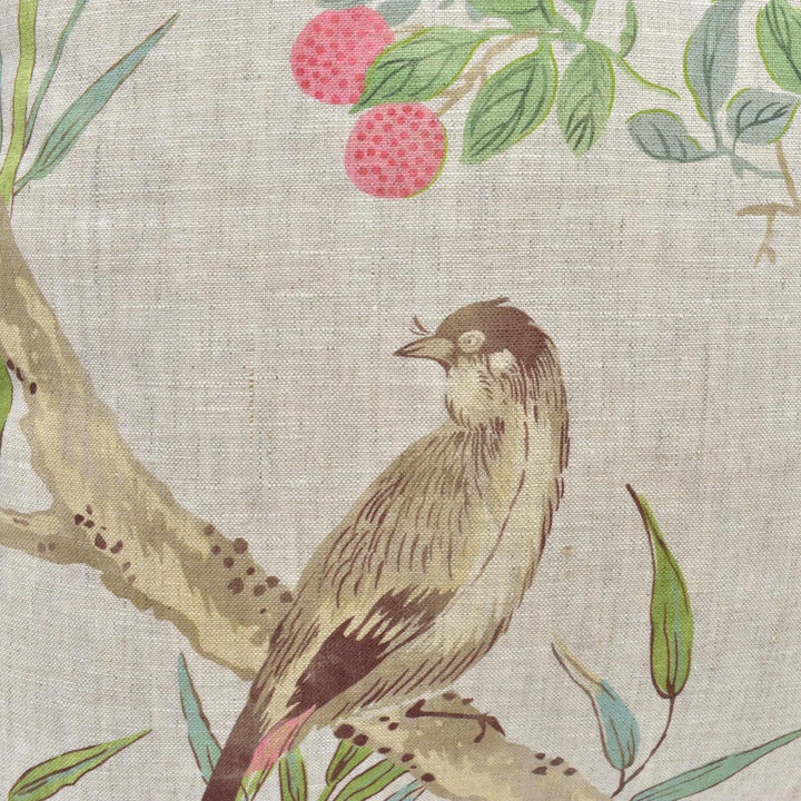A close-up of a bird perched on a branch, with a background of green leaves and pink flowers.