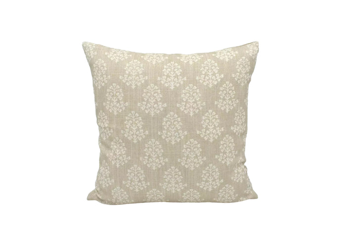 A beige throw pillow with a repeating pattern of white flowers or leaves is displayed against a white background.