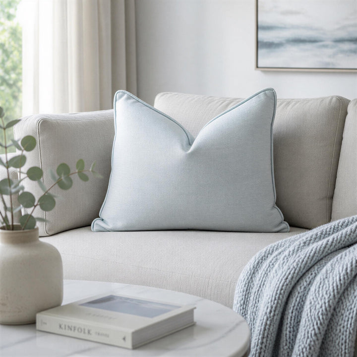 a cozy living room with a beige sofa, a white coffee table, and a decorative plant in a white vase.