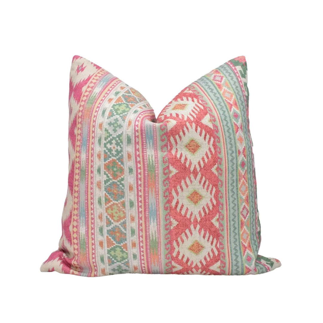 A colorful throw pillow with a pattern of stripes and geometric shapes in shades of pink, green, and white.