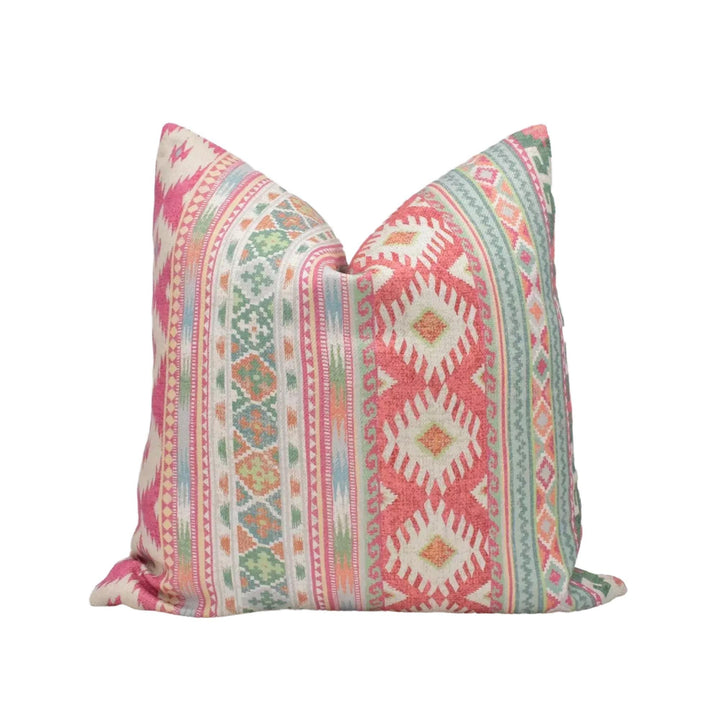 A colorful throw pillow with a pattern of stripes and geometric shapes in shades of pink, green, and white.