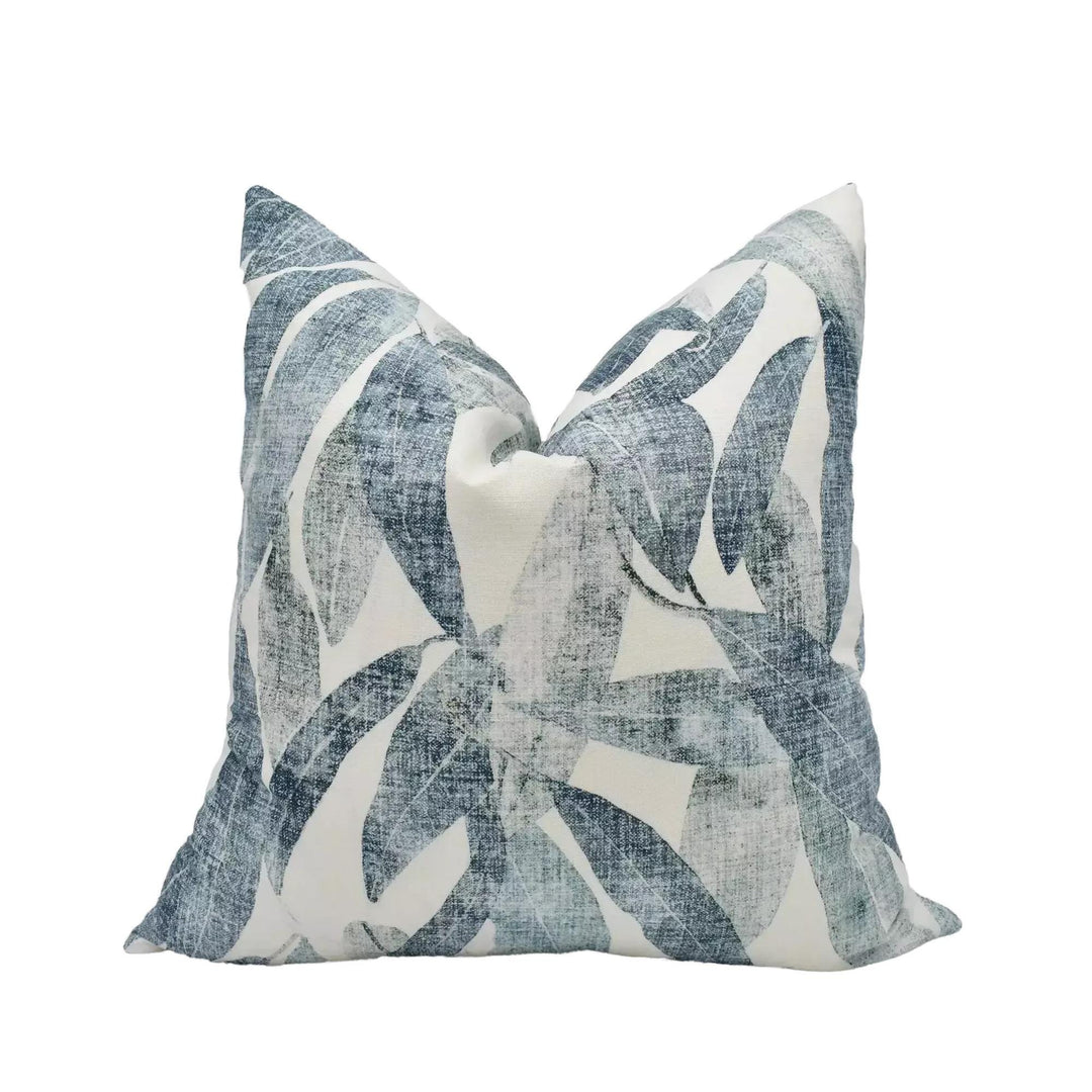 A decorative pillow with a leafy pattern in shades of blue and white is displayed against a white background.