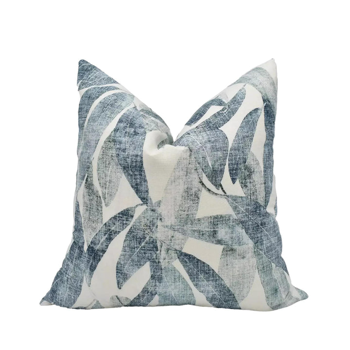 A decorative pillow with a leafy pattern in shades of blue and white is displayed against a white background.