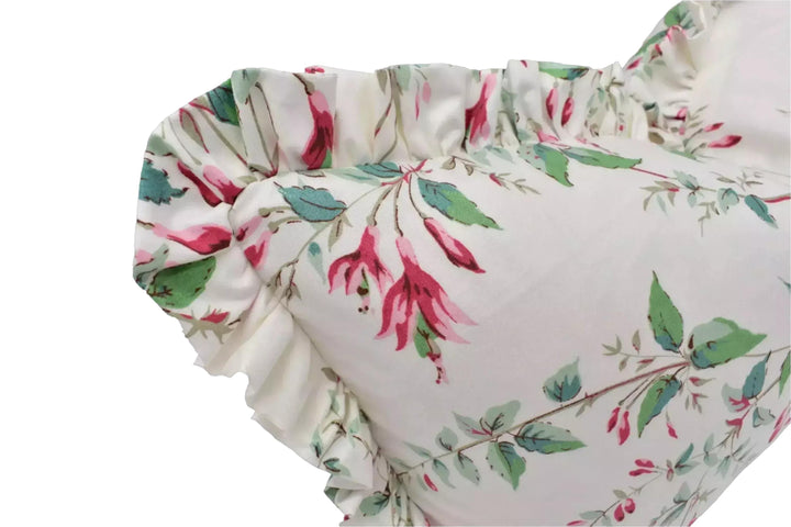A close-up view of a white pillow with a floral print, featuring a ruffled edge and a vibrant pink and green color scheme.