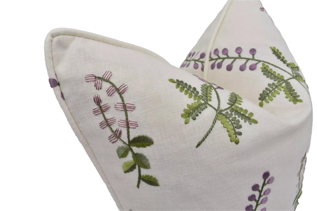 a close-up view of a white fabric with a floral pattern, featuring green leaves and purple flowers.