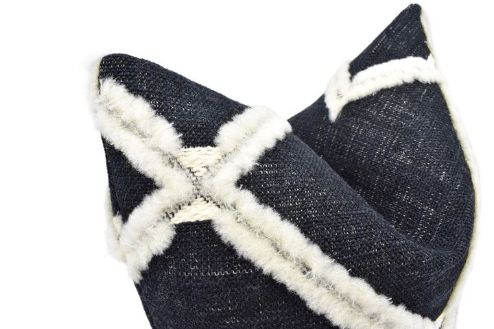 A close-up image of a black and white fabric with a white fur trim, resembling a decorative pillow or cushion.