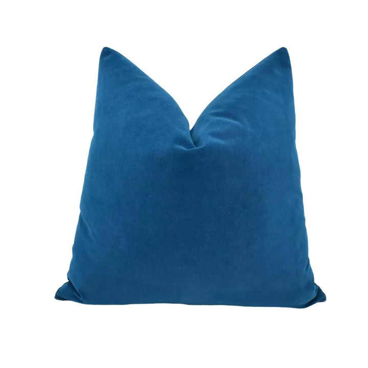 A single, solid blue velvet pillow against a white background.