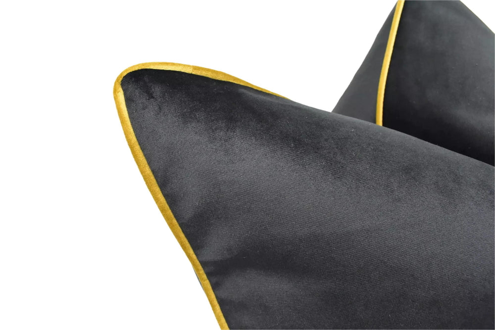 A close-up view of a black velvet pillow with a gold trim, set against a white background.