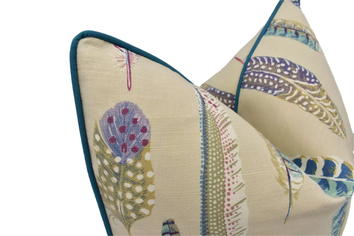a close-up view of a decorative pillow with a pattern of colorful feathers and dots on a beige background.