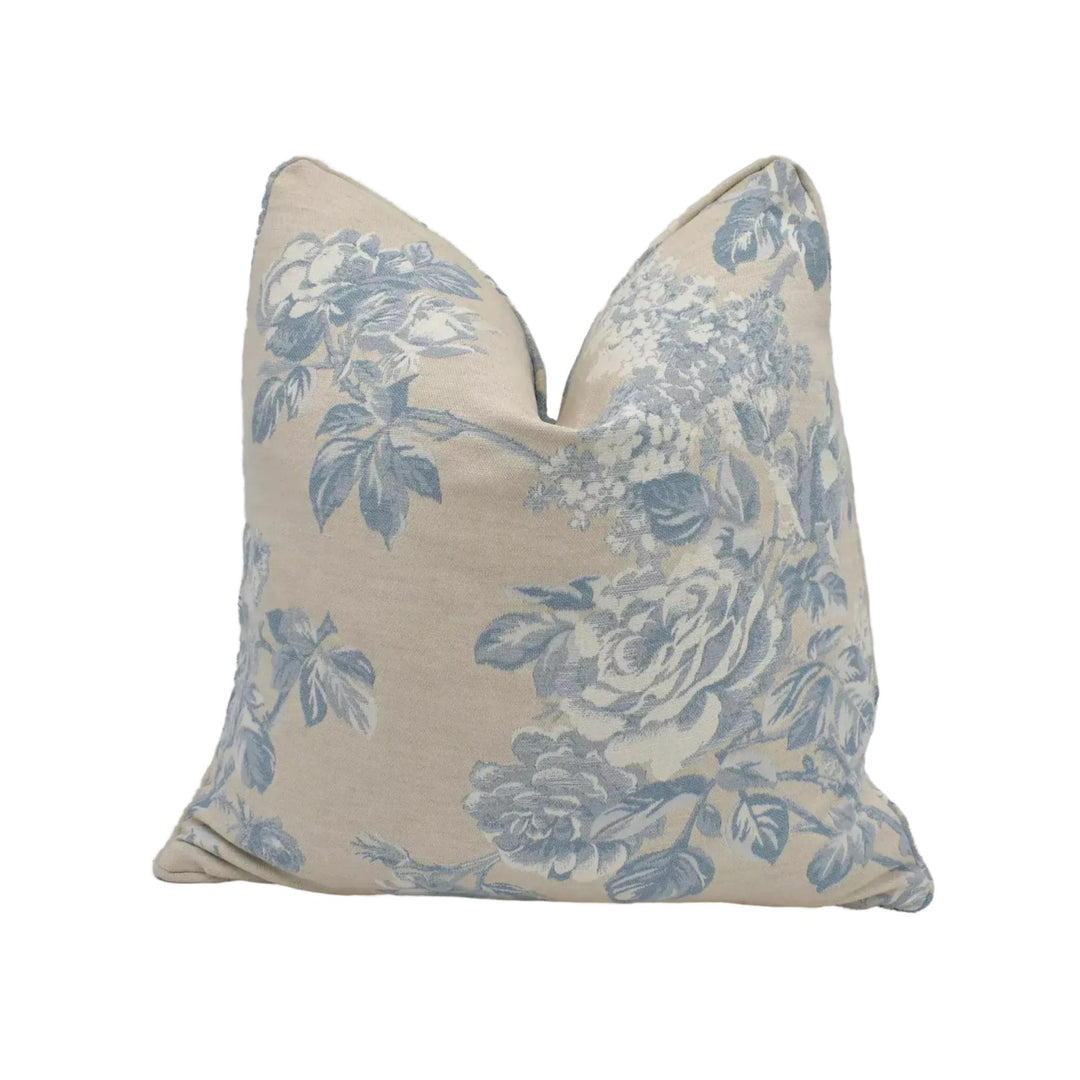 A beige pillow with a floral pattern in shades of blue and white.
