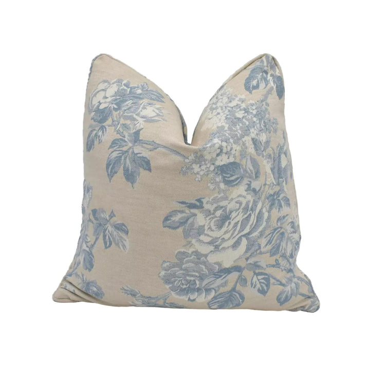 A beige pillow with a floral pattern in shades of blue and white.