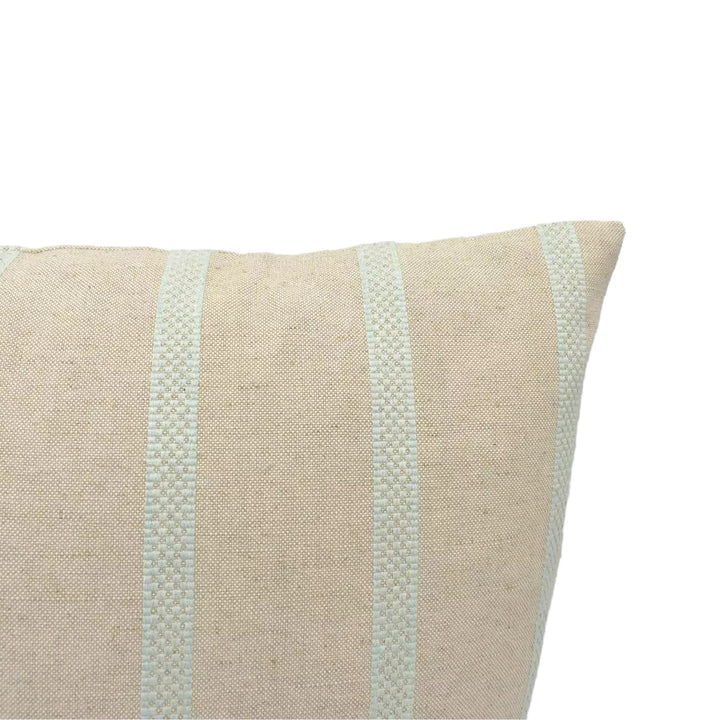 A beige pillow with a striped pattern is shown against a plain white wall.