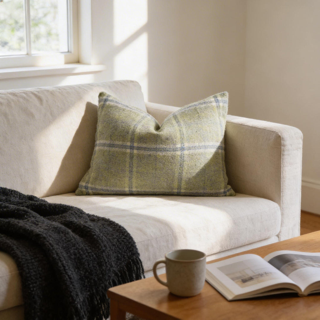 a cozy living room with a beige sofa, a black throw blanket, and a wooden coffee table with a mug and an open book.