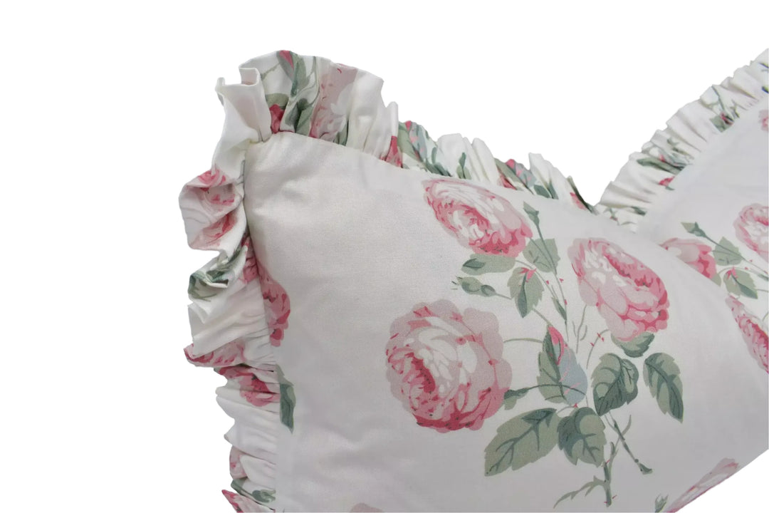 A close-up view of a white pillow with a floral print, featuring a ruffled edge and pink flowers.