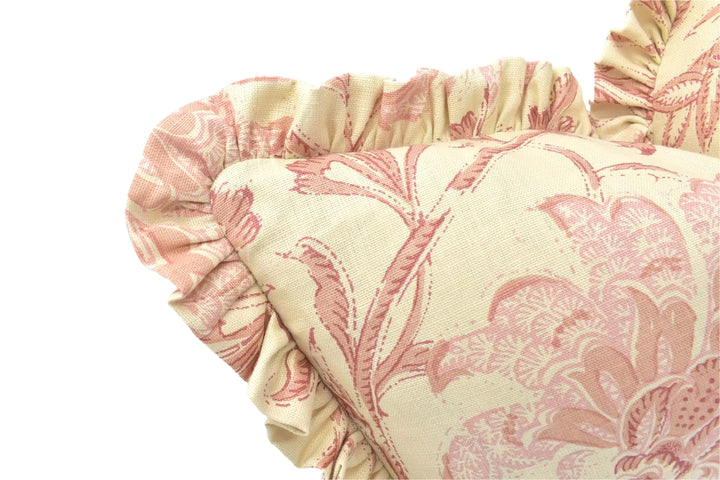 a close-up view of a decorative pillow with a floral pattern in shades of pink and yellow. The pillow has a ruffled edge and a ruffled collar, giving it a charming and elegant appearance.