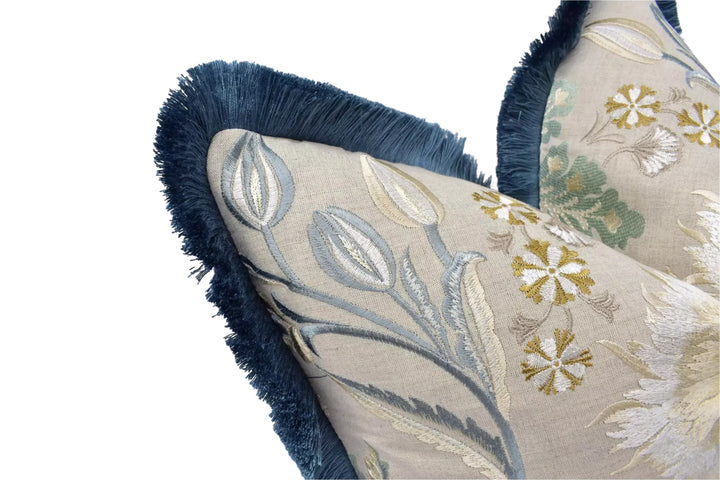 a close-up view of a decorative pillow with a floral pattern and a blue fringe trim.