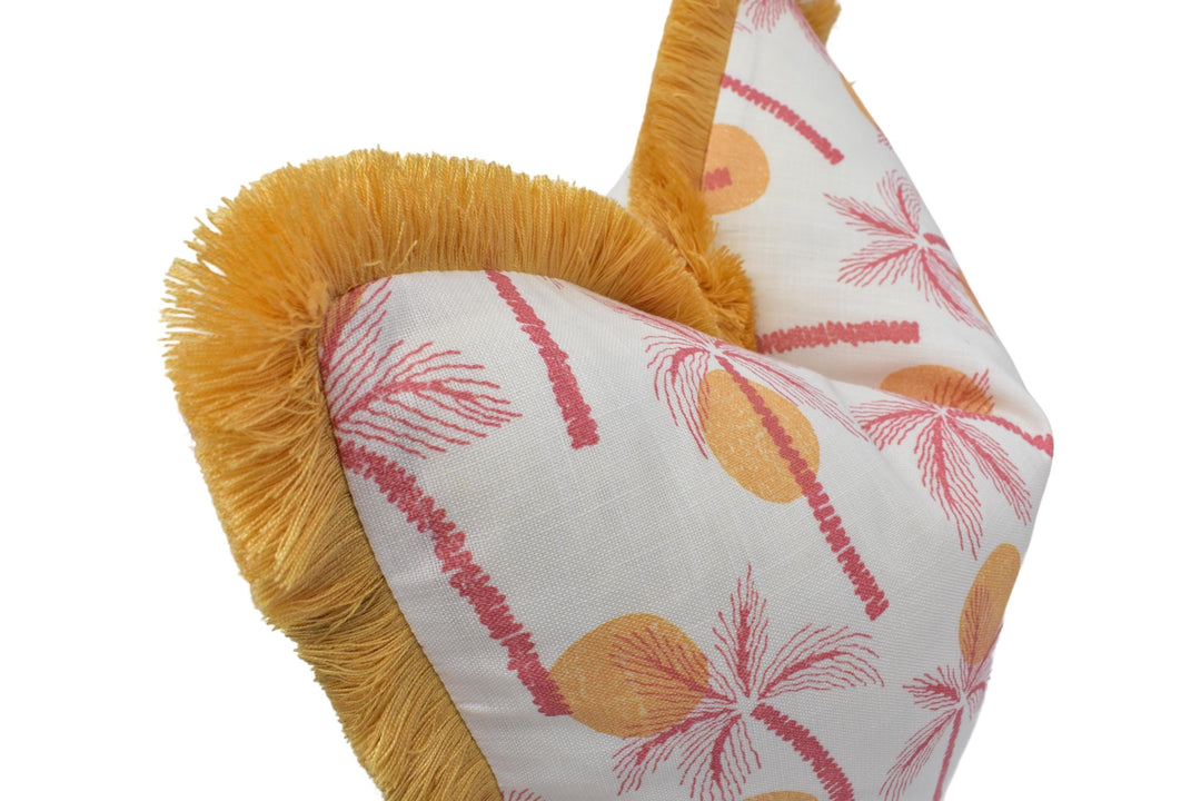 a close-up view of a decorative pillow with a palm tree pattern and a yellow fringe.