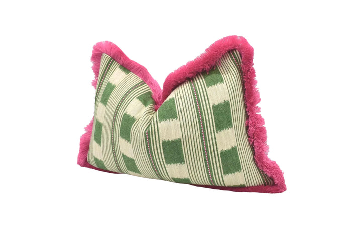 A decorative pillow with a green and white striped pattern and a pink fringe around the edges, placed on a white surface.