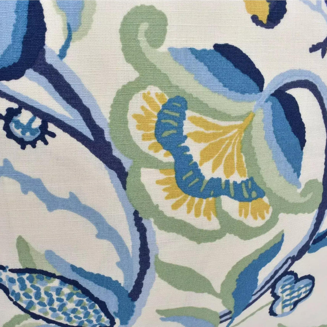 The image is a close-up of a fabric with a floral pattern in shades of blue, green, and yellow. The pattern features various shapes and designs, including flowers, leaves, and other organic elements. The fabric appears to be a textile, possibly a cushion cover or a piece of clothing.