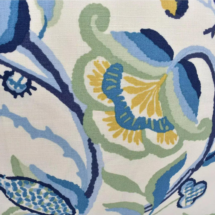 The image is a close-up of a fabric with a floral pattern in shades of blue, green, and yellow. The pattern features various shapes and designs, including flowers, leaves, and other organic elements. The fabric appears to be a textile, possibly a cushion cover or a piece of clothing.