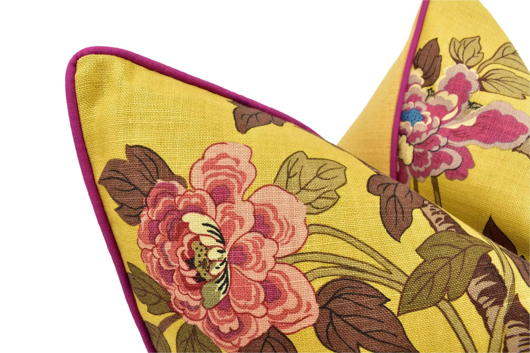a close-up view of two yellow pillows with a floral pattern. The pillows have a vibrant yellow color and are adorned with pink and green floral designs. The pillows are positioned side by side, with the one on the left slightly overlapping the one on the right.