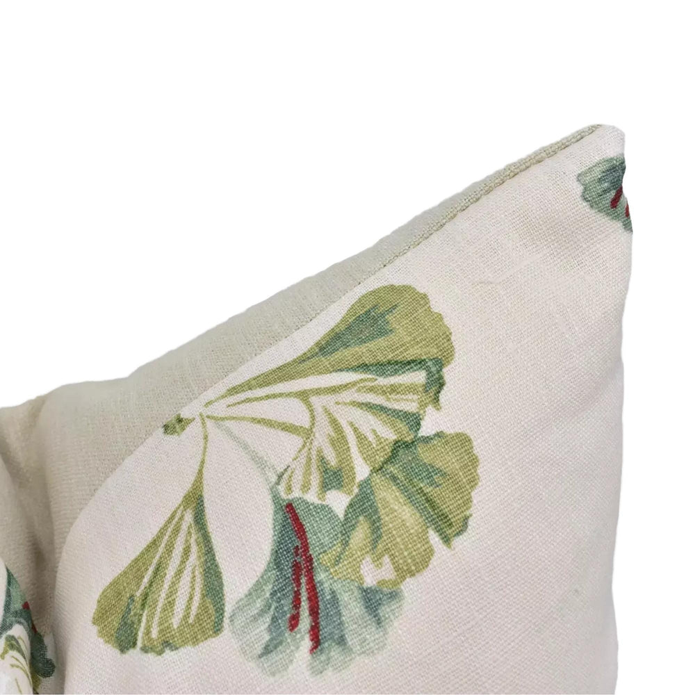 A close-up view of a white fabric with a green and red floral pattern, featuring a large green leaf and a red stem.