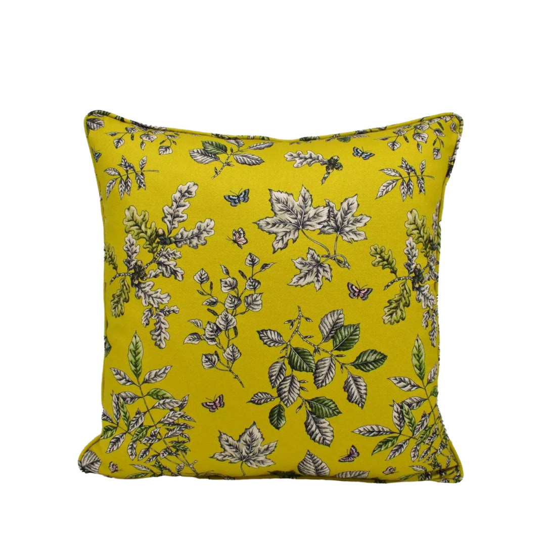 A square throw pillow with a vibrant yellow background and a repeating pattern of white and green leaves and flowers.
