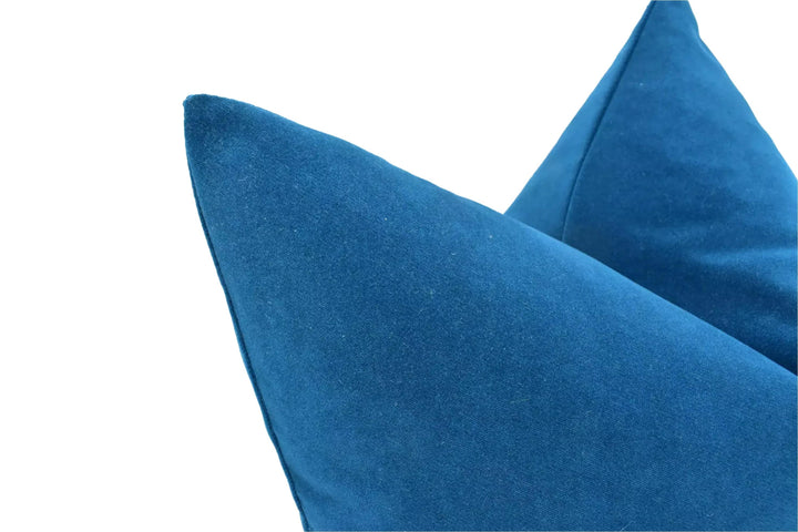 A close-up view of a blue velvet pillow against a white background.
