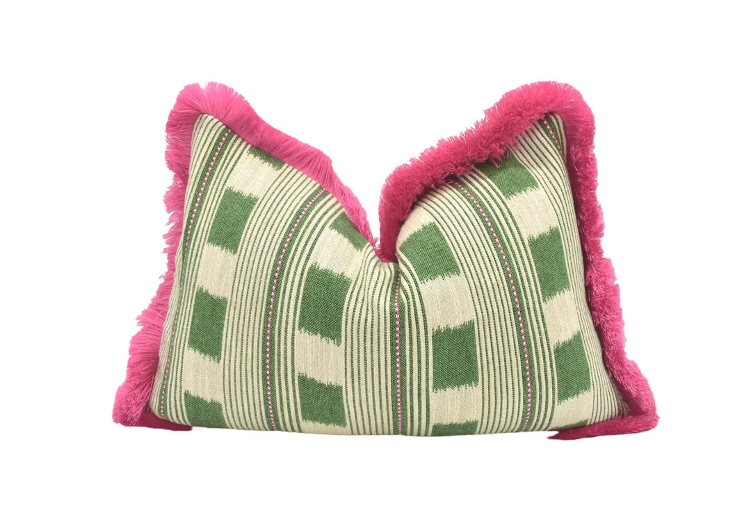 A decorative pillow with a green and white striped pattern and a pink fringe around the edges, placed on a white surface.