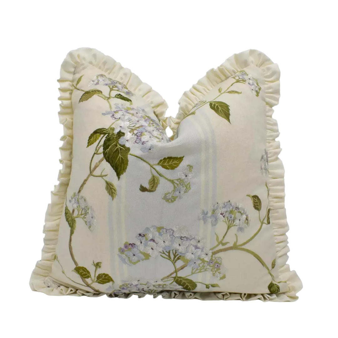 A decorative white pillow with a floral pattern and ruffled edges.