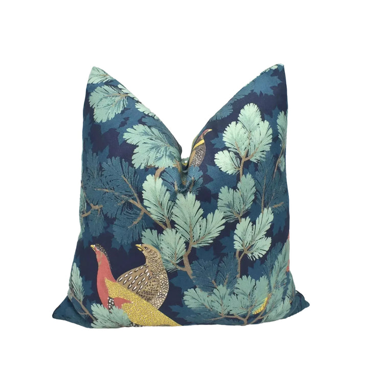 A decorative pillow with a blue and green leaf pattern and a bird design, placed on a white surface.