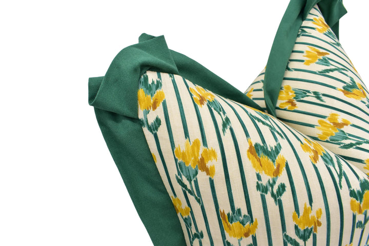 a close-up view of a decorative pillow with a floral pattern in shades of green and yellow. The pillow has a green trim and a white background, creating a visually appealing contrast.